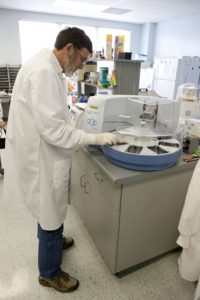 Man with brown hair in lab coat putting tray into machine