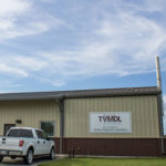 Photo of tan metal and red brick TVMDL Poultry lab building in Gonzales with a white ford truck park in the front.