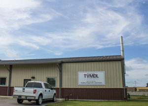 Photo of tan metal and red brick TVMDL Poultry lab building in Gonzales with a white ford truck park in the front.