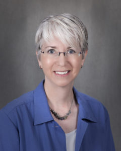 Portrait of a woman with short hair in glasses, a blue jacket and white blouse
