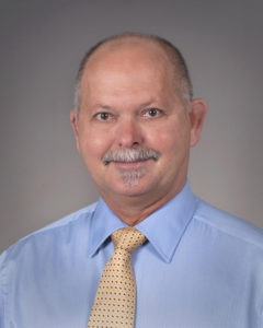 Portrait of man white white hair and facial hair in blue shirt and yellow tie