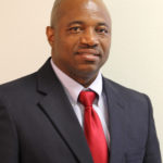 Portrait of a African American man in a black suit, white button down and red tie.