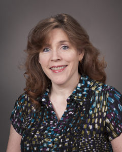 Portrait of a woman with light brown curled hair and blue eyes in a black multicolored blouse