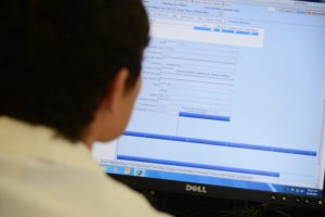 man with short dark hair wearing a lab coat looking at a computer monitor