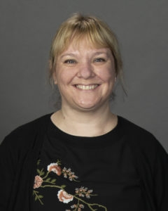 Woman with blonde hair wearing a black floral shirt smiling for a professional portrait
