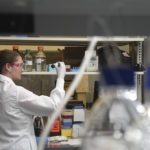 Woman in white laboratory coat examines bottle of reagent