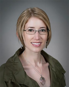 Woman with blonde hair, glasses, and green shirt posing for portrait
