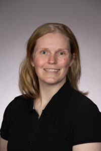 White woman with blonde hair and a black shirt posing in front of a gray background