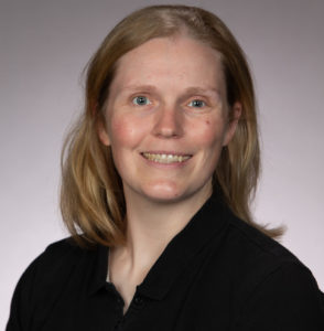 White woman with blonde hair and a black shirt posing in front of a gray background
