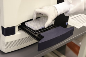Hand in a white glove putting a sample into a diagnostic machine