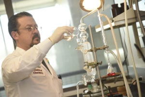 man in white lab coat pour liquid into chemistry equipment