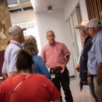 Group of individuals being led on laboratory tour by man in pink short sleeve shirt