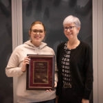 woman with glasses in white sweatshirt accepts plaque from woman in black cardigan and white hair