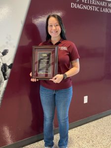 Woman in maroon shirt posing with an award plaque