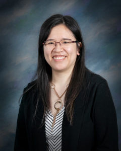 woman with black hair, glasses, and a black blazer coat smiling for a professional portrait