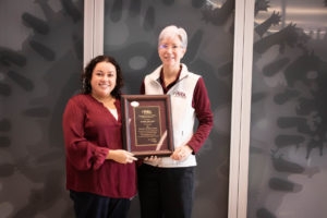 woman with black hair and maroon shirt accepting award from woman in white vest and white hair