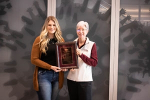woman with blonde hair and brown cardigan accepting award from woman in white vest and white hair