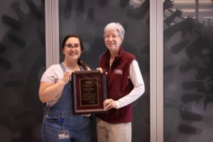 woman white white shirt and overalls accepting award from woman in maroon vest and white hair