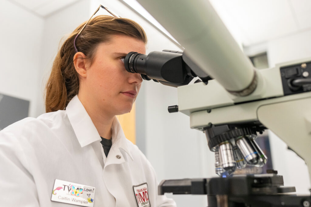 woman with brown hair and white lab coat looking through microscope