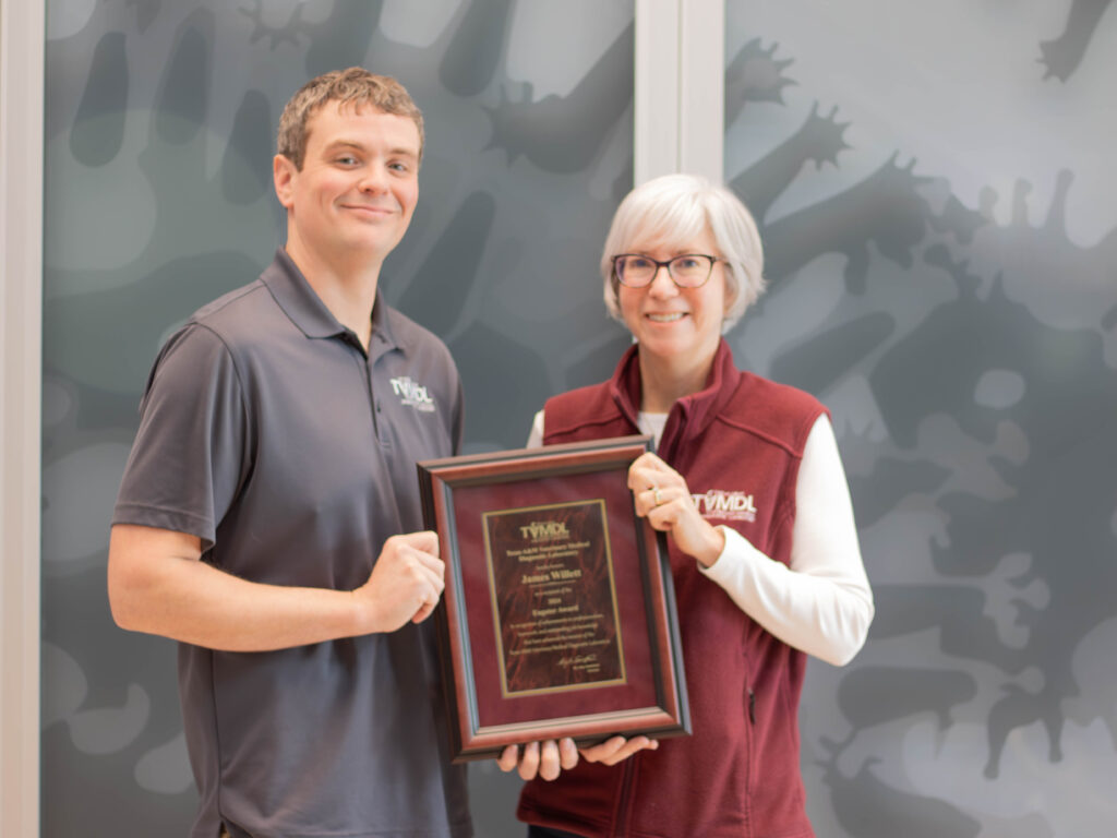 man in gray shirt accepting award plaque from women in maroon vest and white shirt.