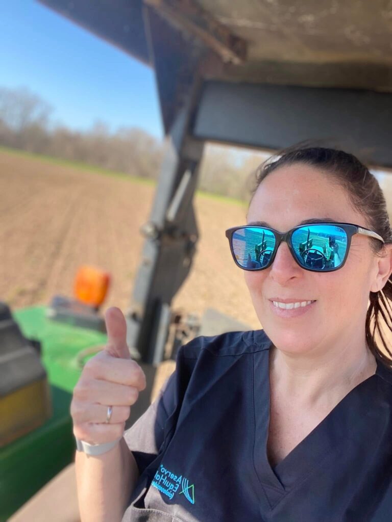 woman wearing black shirt and sunglasses giving a thumbs up while driving a tractor