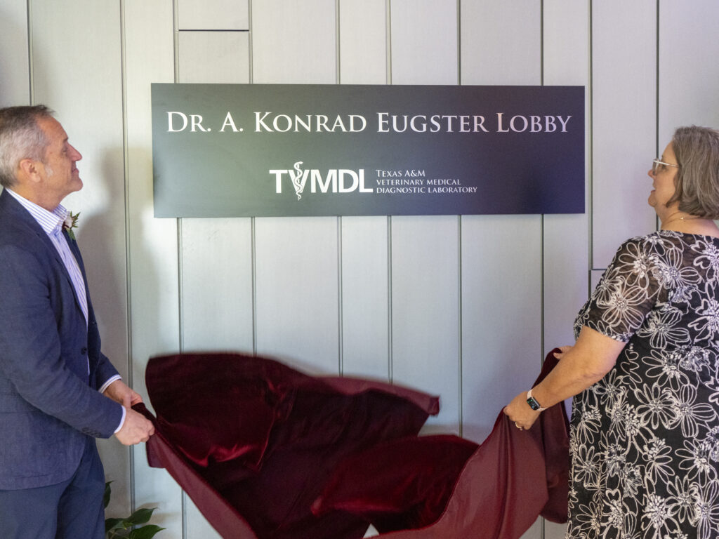 man in blue suit and woman in floral dress unveil a sign in a lobby